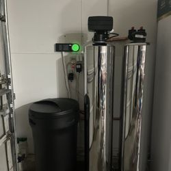 A water softener is sitting next to a trash can in a bathroom.