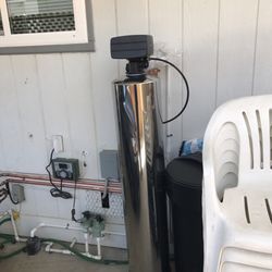 A stainless steel water softener is sitting next to a white chair.