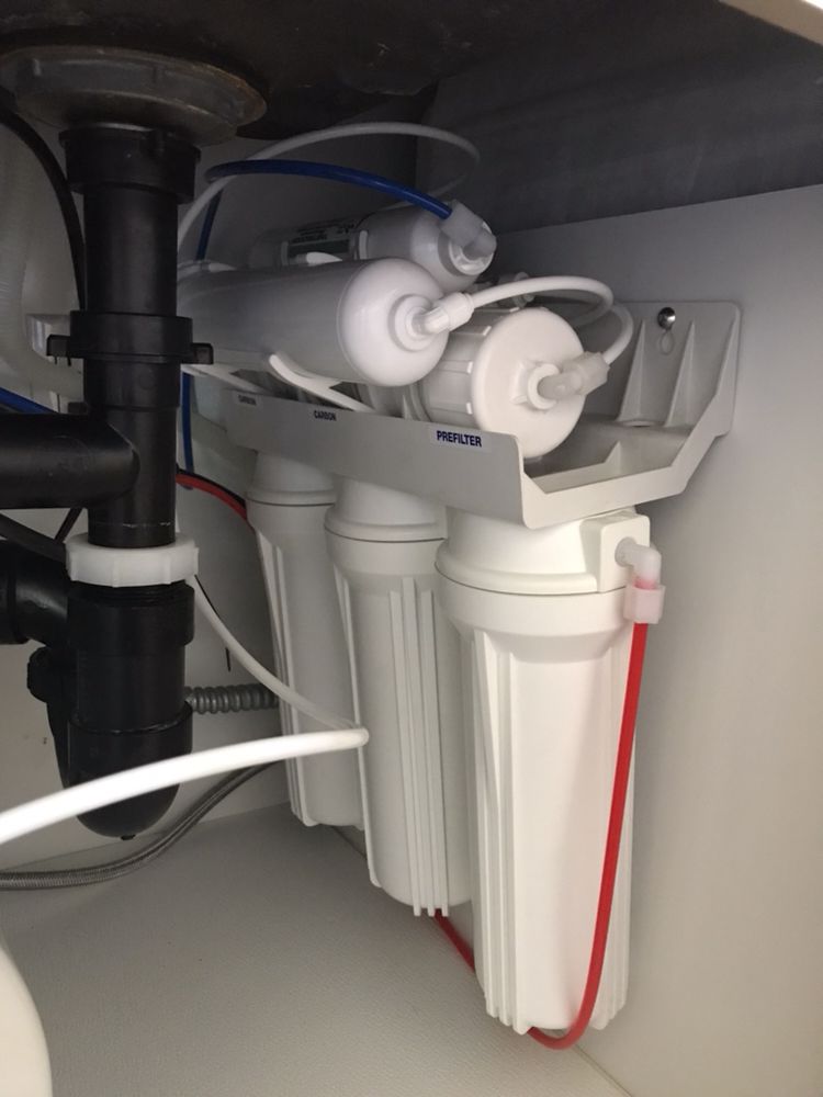 A water filter is under a sink in a kitchen.