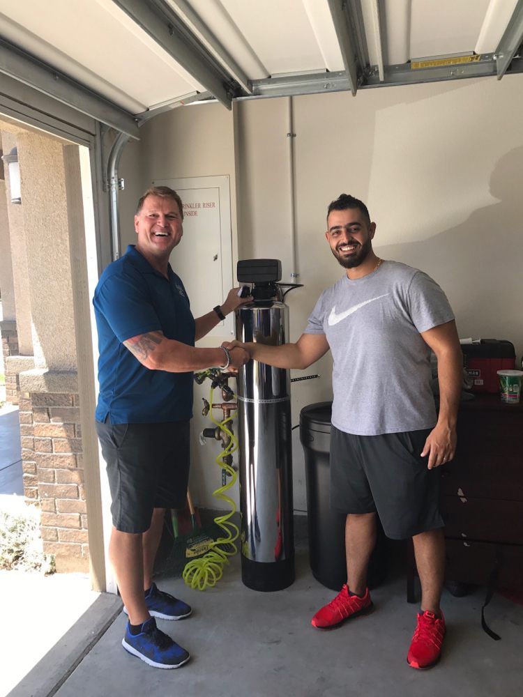 Two men are shaking hands in front of a water filter in a garage.