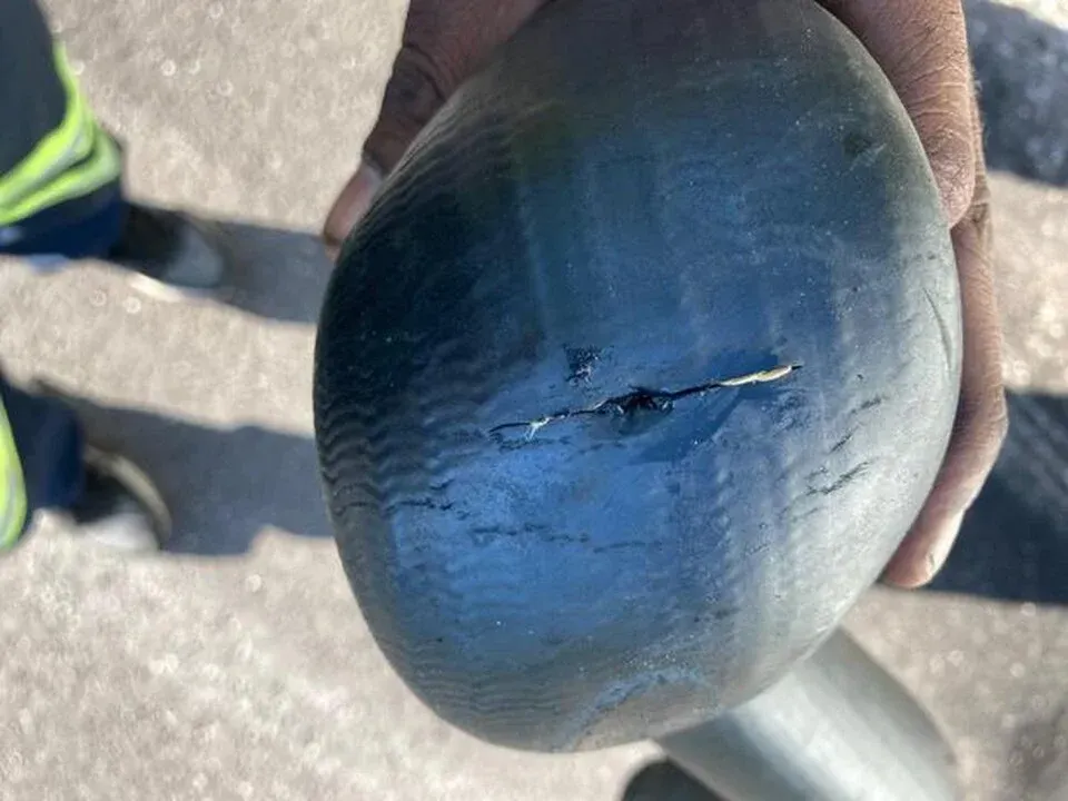 Close-up of a cracked, black rubber object held by a person. Asphalt and shoes are visible in the background.