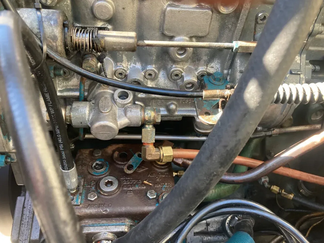 Close-up of an engine's fuel system with metal pipes, fittings, and a valve. Blue and gray components are visible.