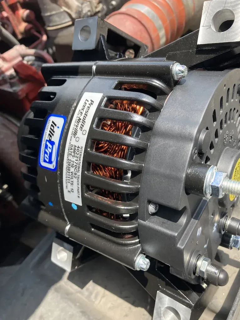Close-up of a black alternator in an engine bay. It has copper wiring and is attached to a metal bracket.