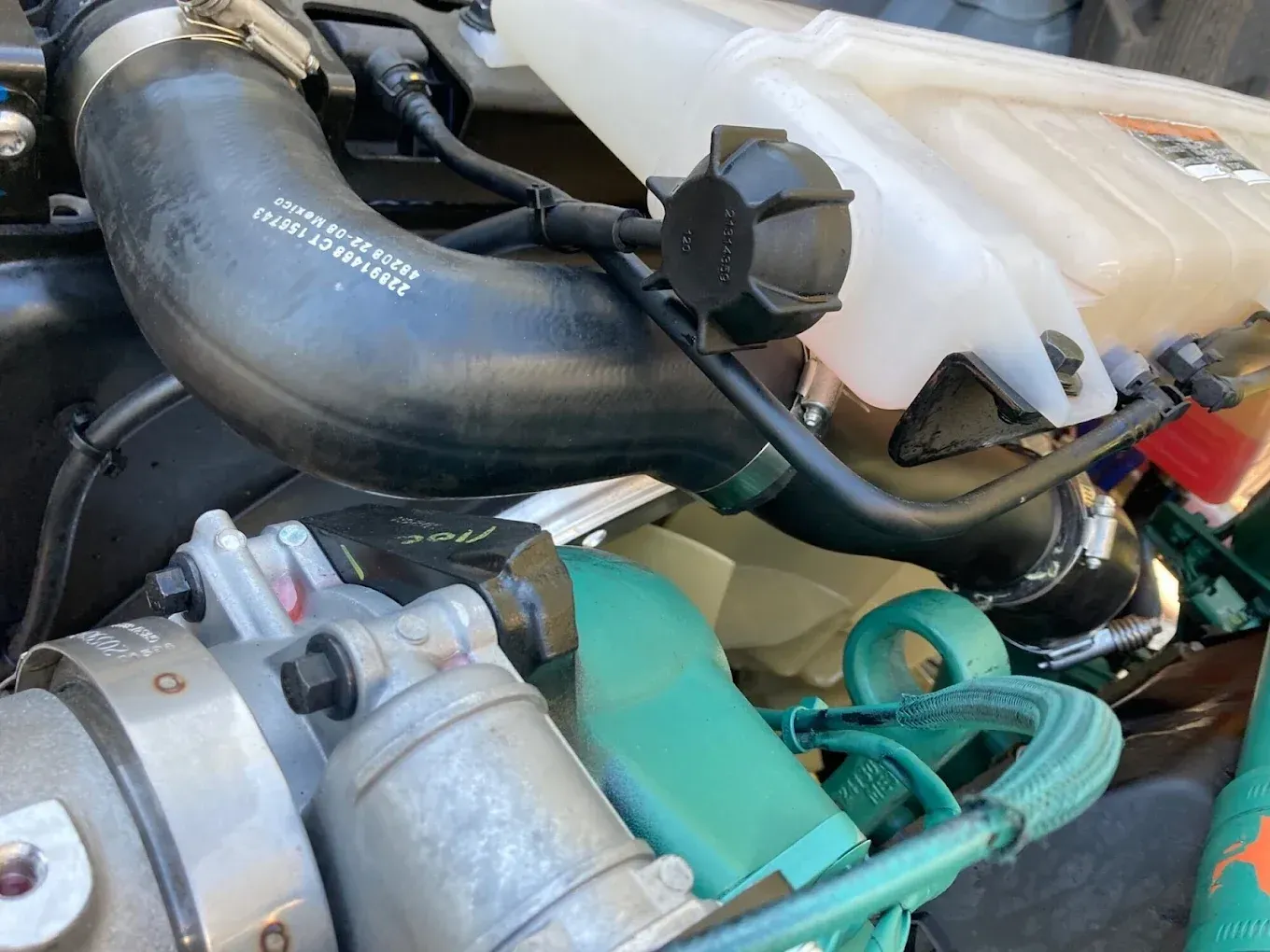 Car engine components including a black hose, coolant reservoir, and metal parts.