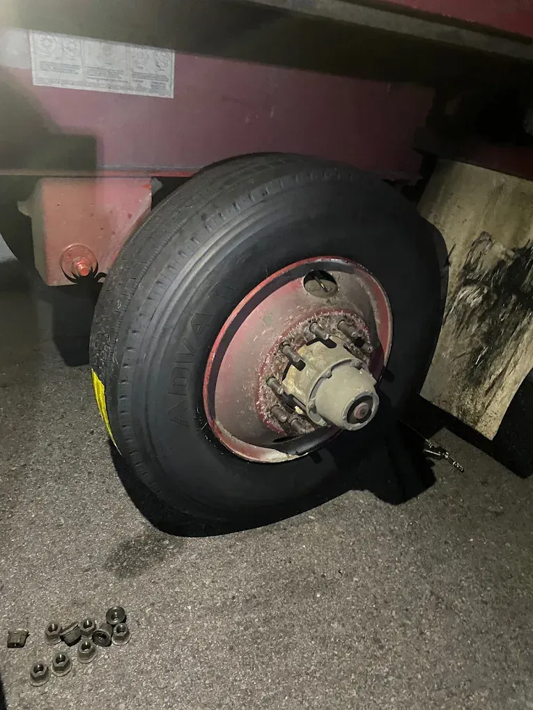 Flat tire on a red trailer; wheel is off the ground, lug nuts in foreground.