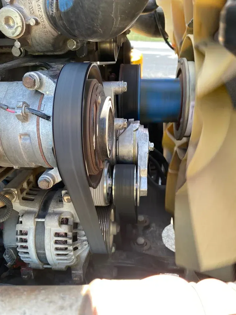 Close-up of a truck engine with belt, alternator, and air conditioning compressor visible.