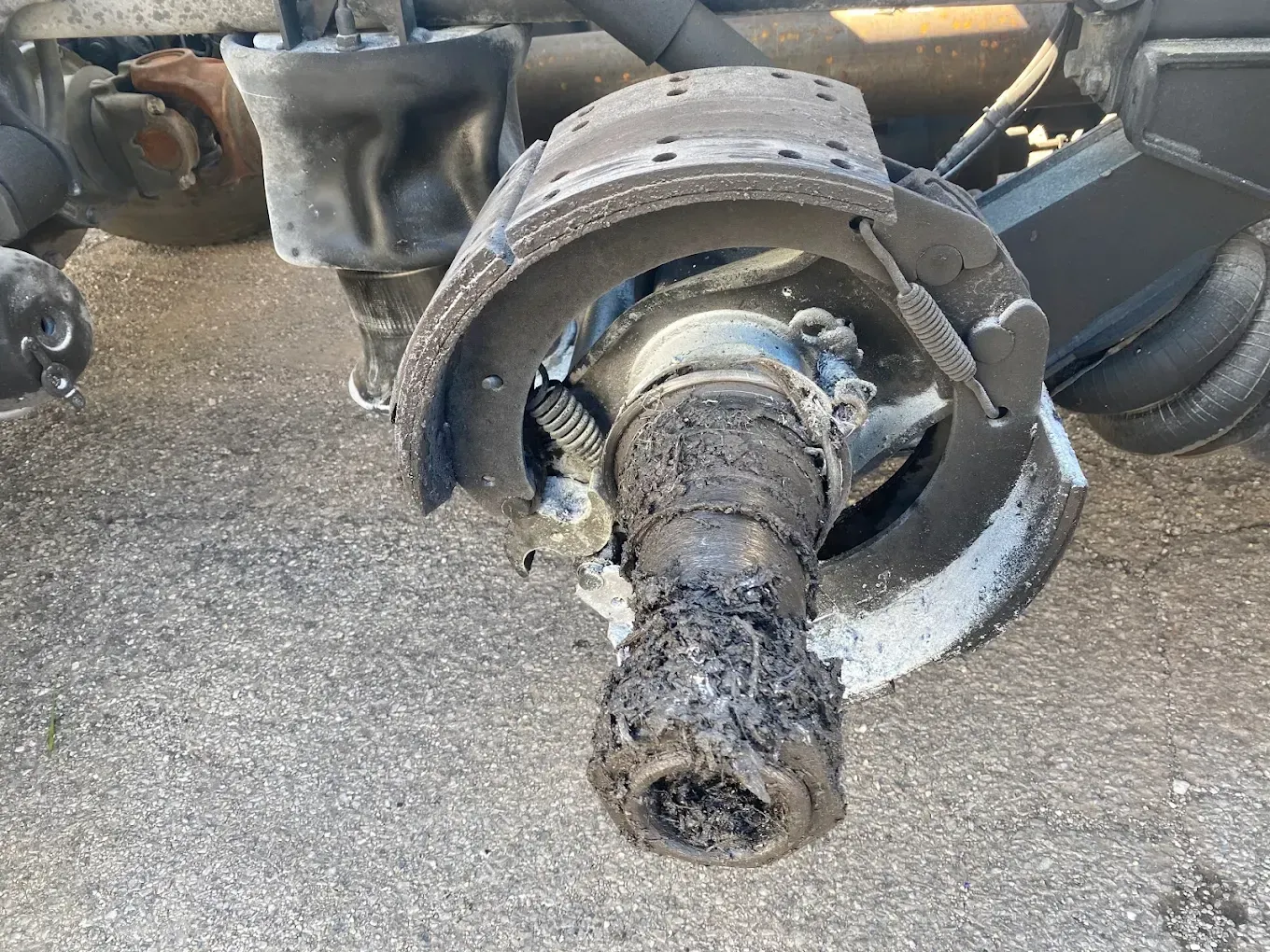 Damaged truck wheel assembly, showing severely worn brake components and axle. Debris and wear present.