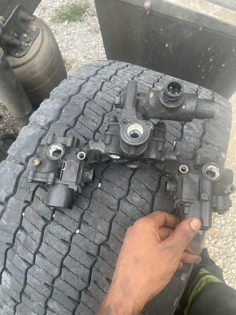 Black hand holding truck air brake valve parts on a worn tire.