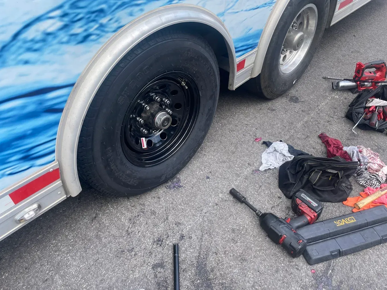 A trailer tire being worked on, tools scattered on the ground.