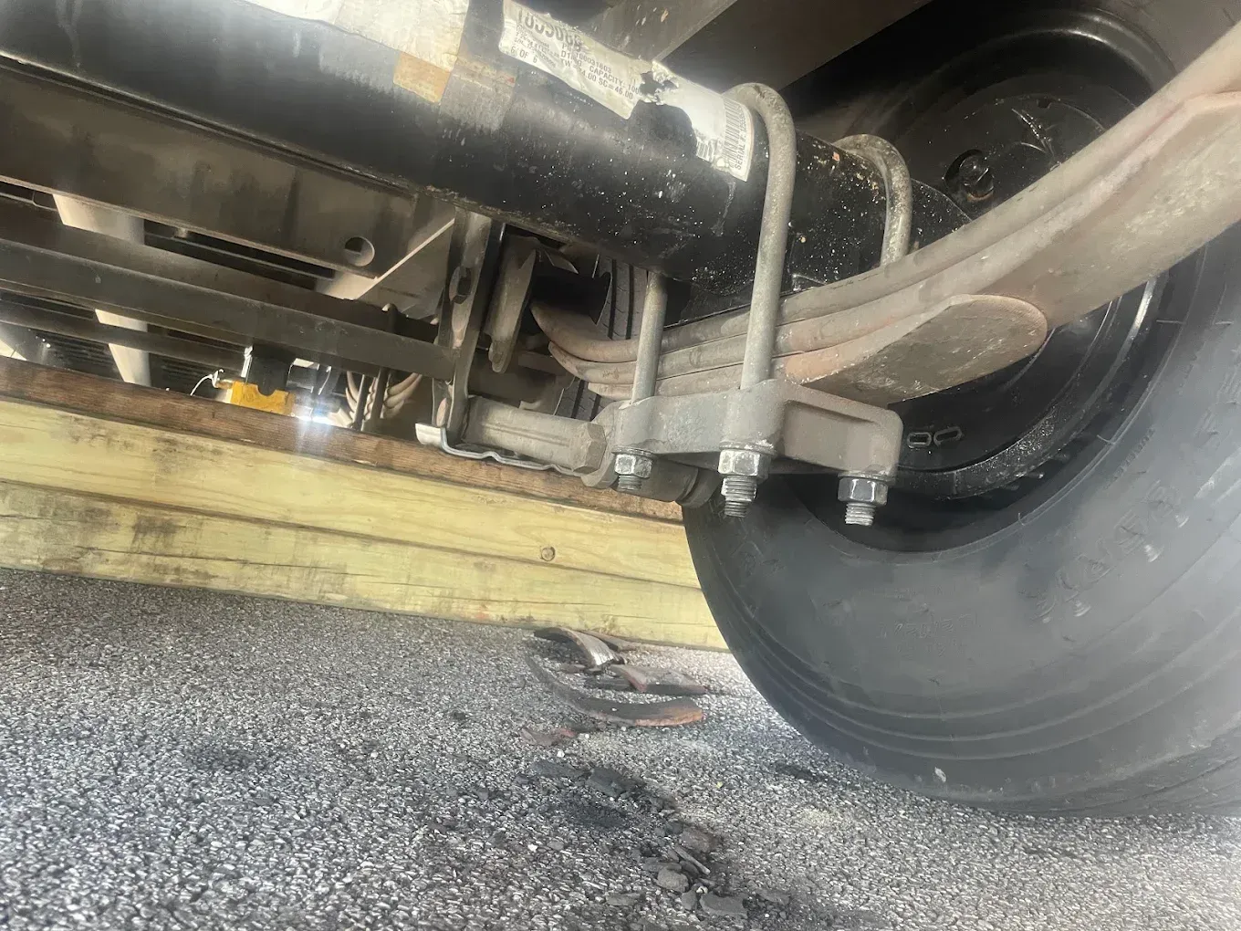 Undercarriage of a vehicle with a leaf spring suspension, wheel, and frame supported by a wooden block.