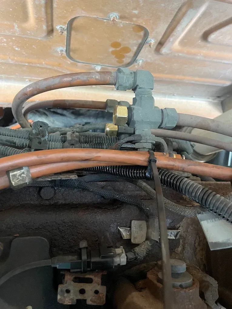 Engine compartment with hoses and brass fittings, likely for fuel or air lines.