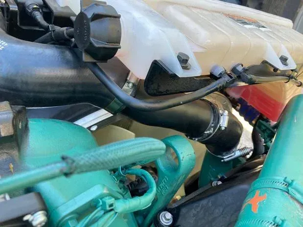 Engine compartment with black hoses and clamps, coolant reservoir, and green-painted components.