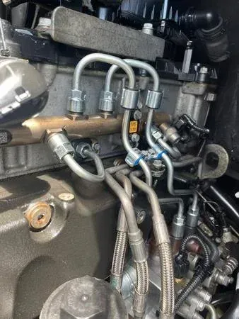 Engine component with fuel lines, possibly for a diesel engine. Steel pipes connect to injectors and a fuel rail.