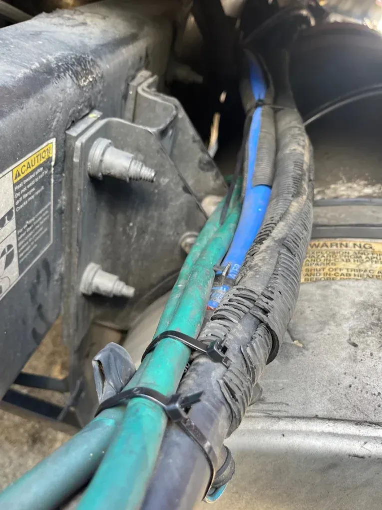 Bundle of blue and green hoses and wires secured by a black zip tie near a black engine component.