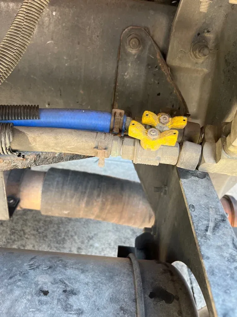 Yellow valve controls on metal plumbing, with blue and black hoses in a vehicle compartment.