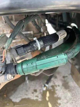 Close-up of car engine wiring harness with black and green connectors, covered in protective mesh, secured with white ties.