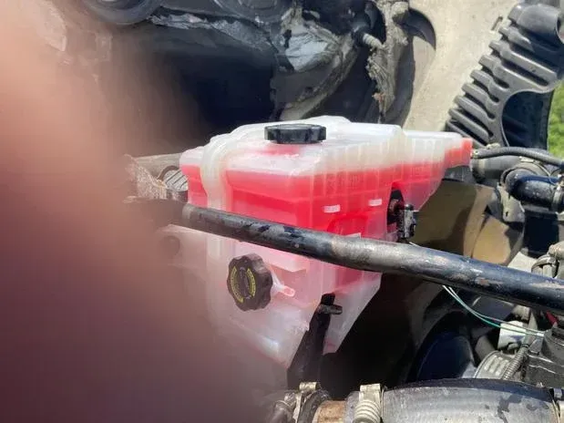 Coolant reservoir filled with pink fluid under the hood of a vehicle.