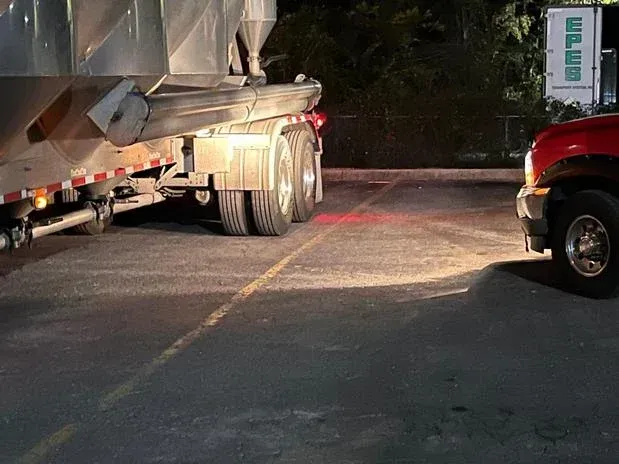 Semi-truck trailer backing up near a red pickup truck in a parking lot at night.