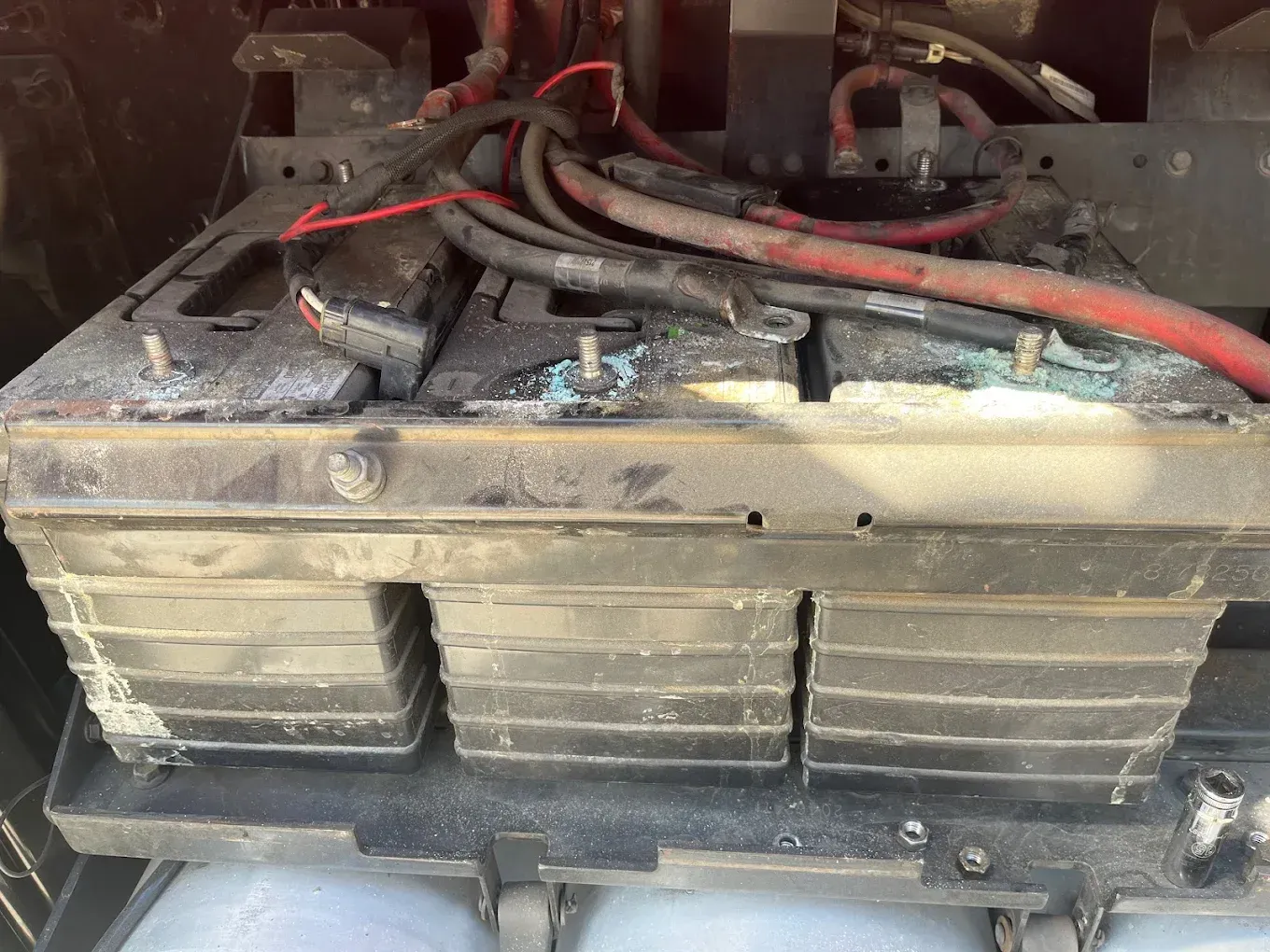 Three vehicle batteries in a black tray, with corrosion and wiring.