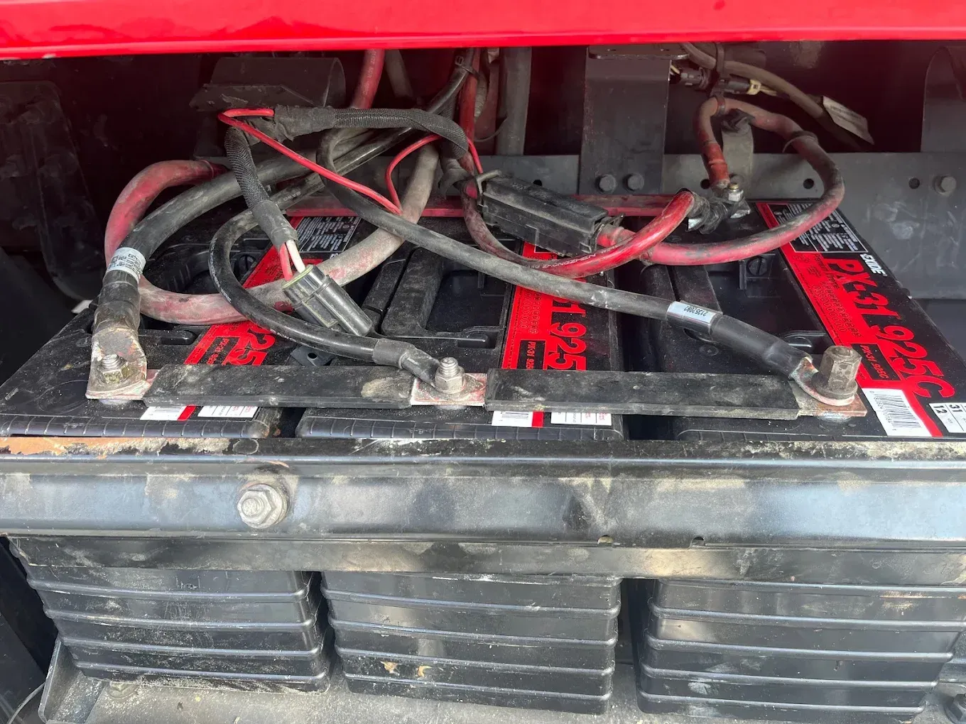 Two black batteries with red cables and terminals inside a red compartment.