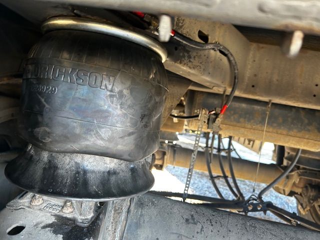 Close-up of hydraulic hoses and fittings connected to a machine. Black and yellow hoses, metal connectors.