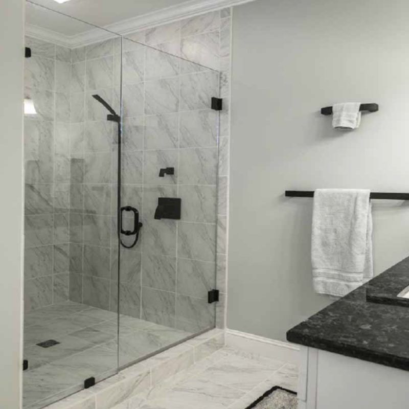 Modern bathroom with glass shower and black fixtures; white and gray marble tiles; towels hanging on wall.