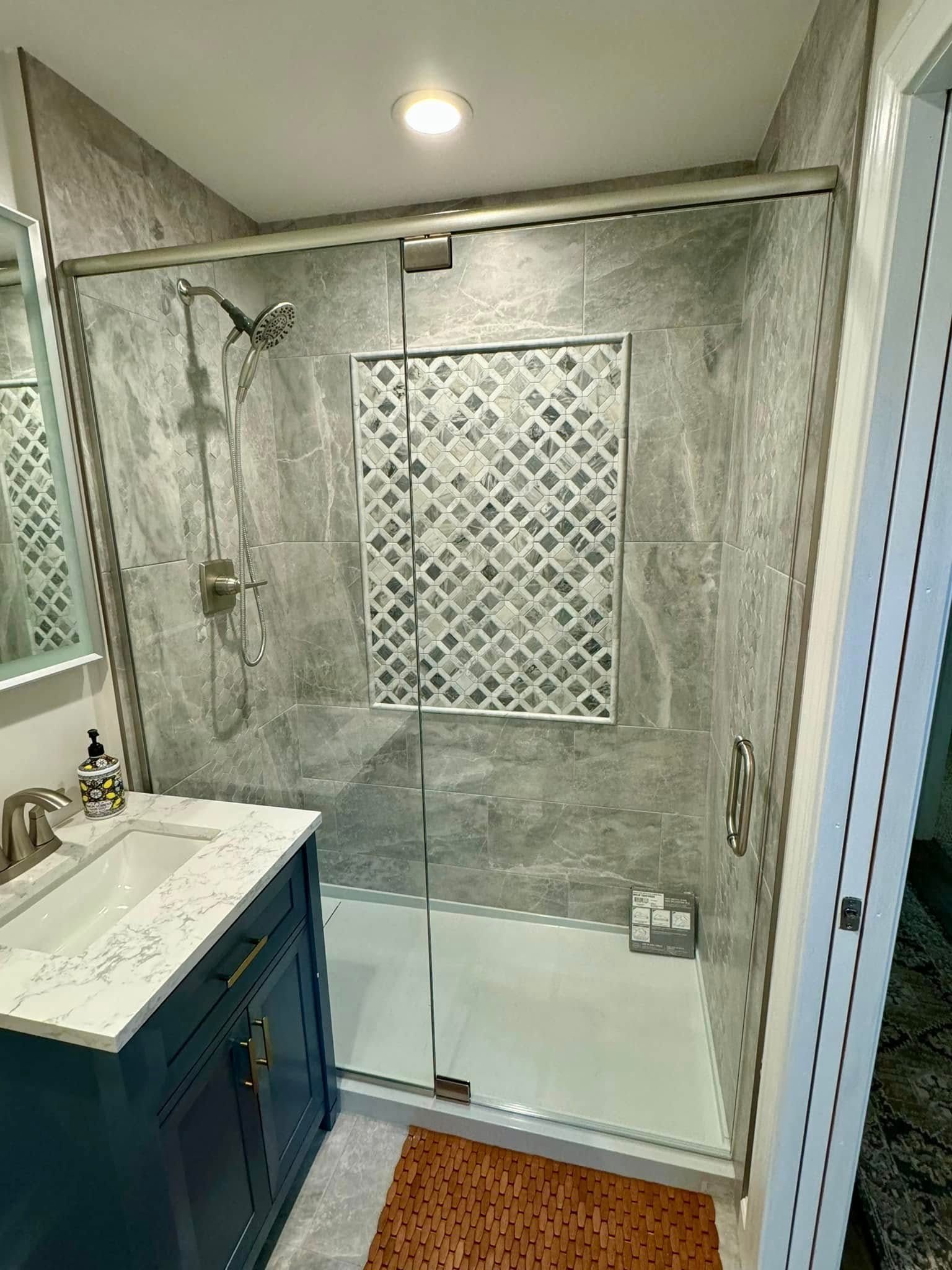 Bathroom with grey stone-like tile shower enclosure and a blue vanity with a white countertop.