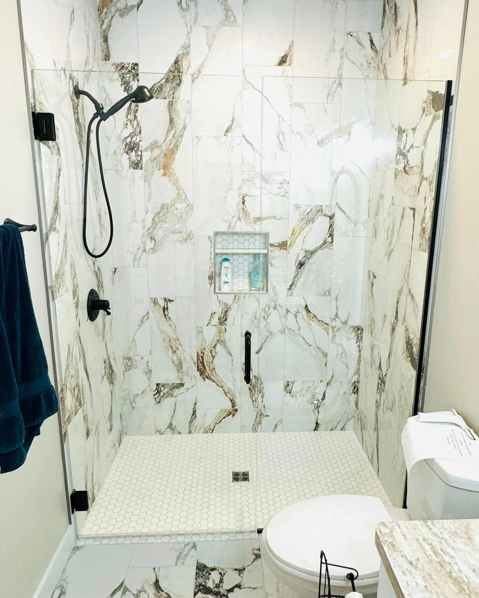 Marble shower with glass doors, black fixtures, and white toilet.