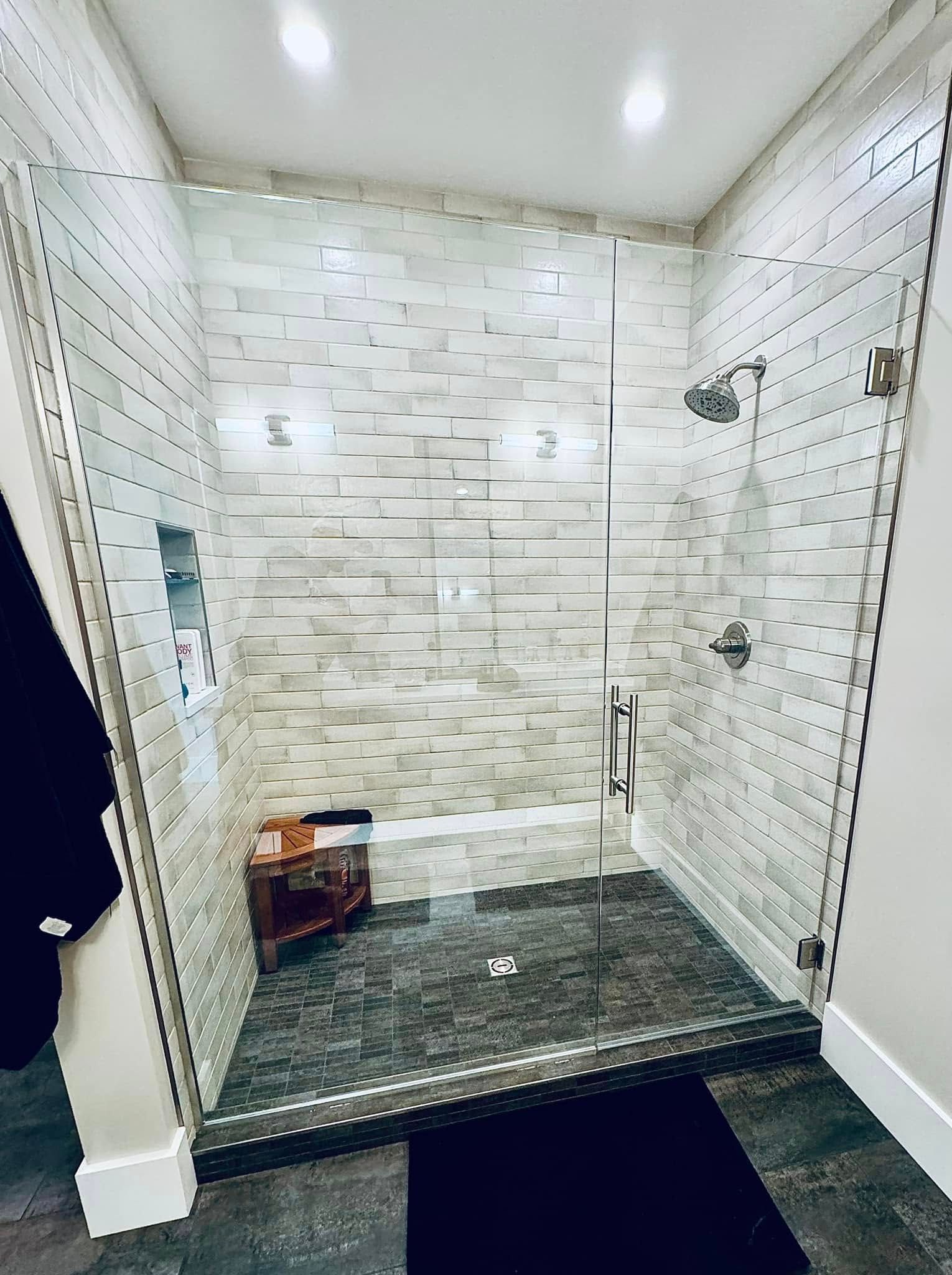 Modern bathroom with a glass shower, white textured tile, and gray floor.