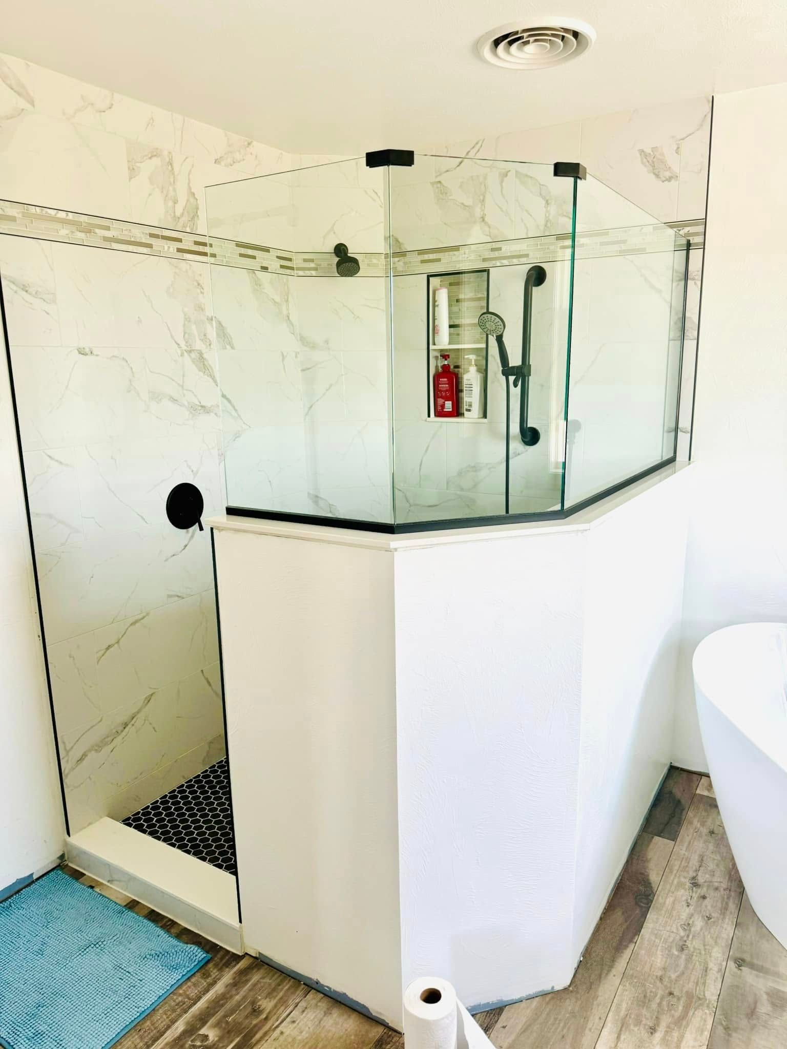 Corner shower with glass doors, white tile, black accents, and a freestanding bathtub.