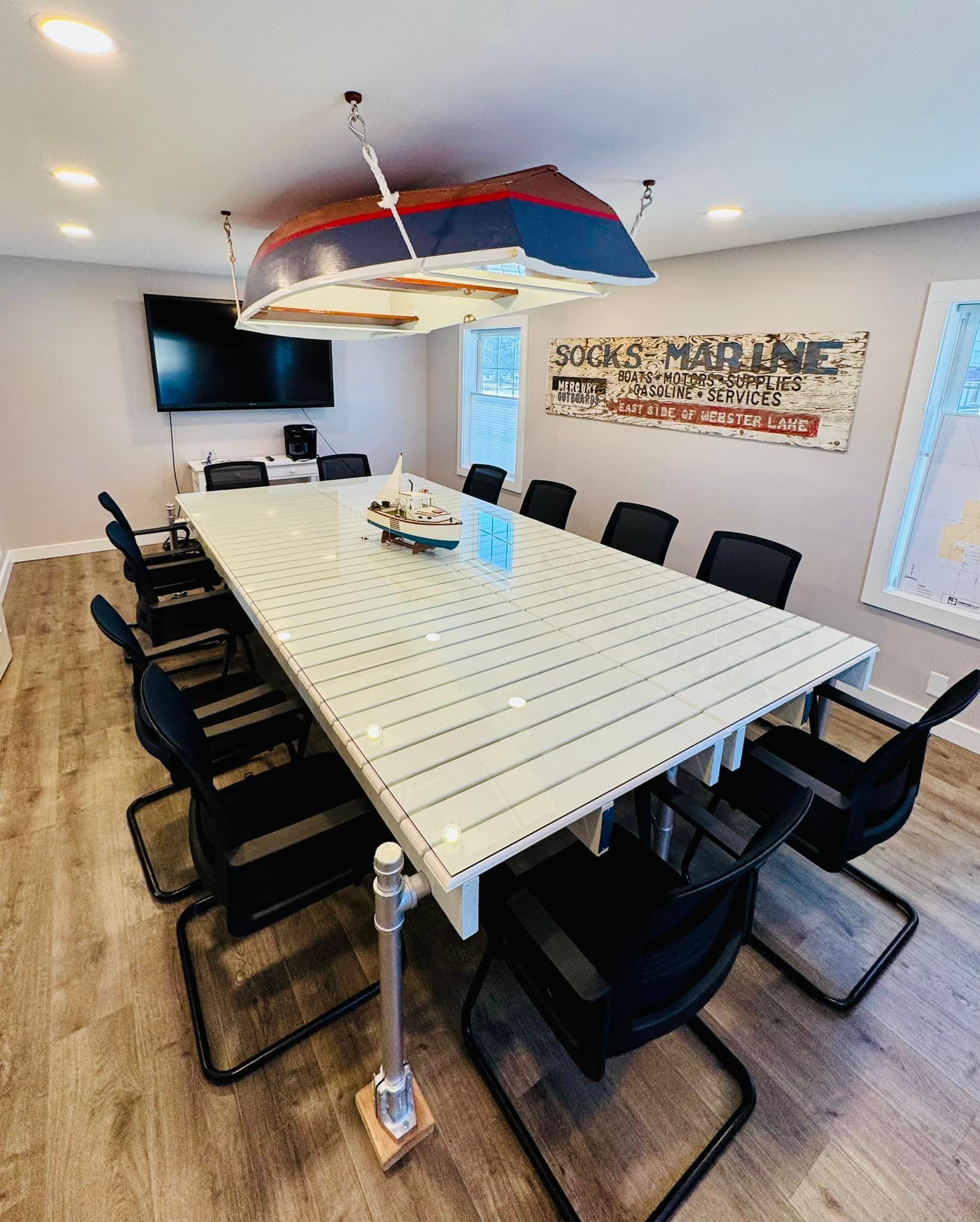 Conference room with white table, black chairs, boat-shaped light fixture, TV, and coastal decor.