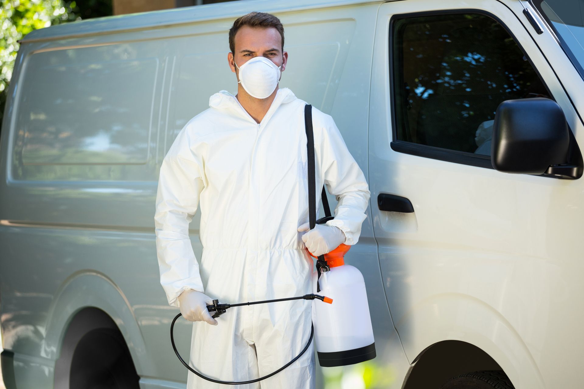 Pest control worker in protective suit with sprayer standing beside service van. Pest control worker in protective suit with sprayer standing beside service van.