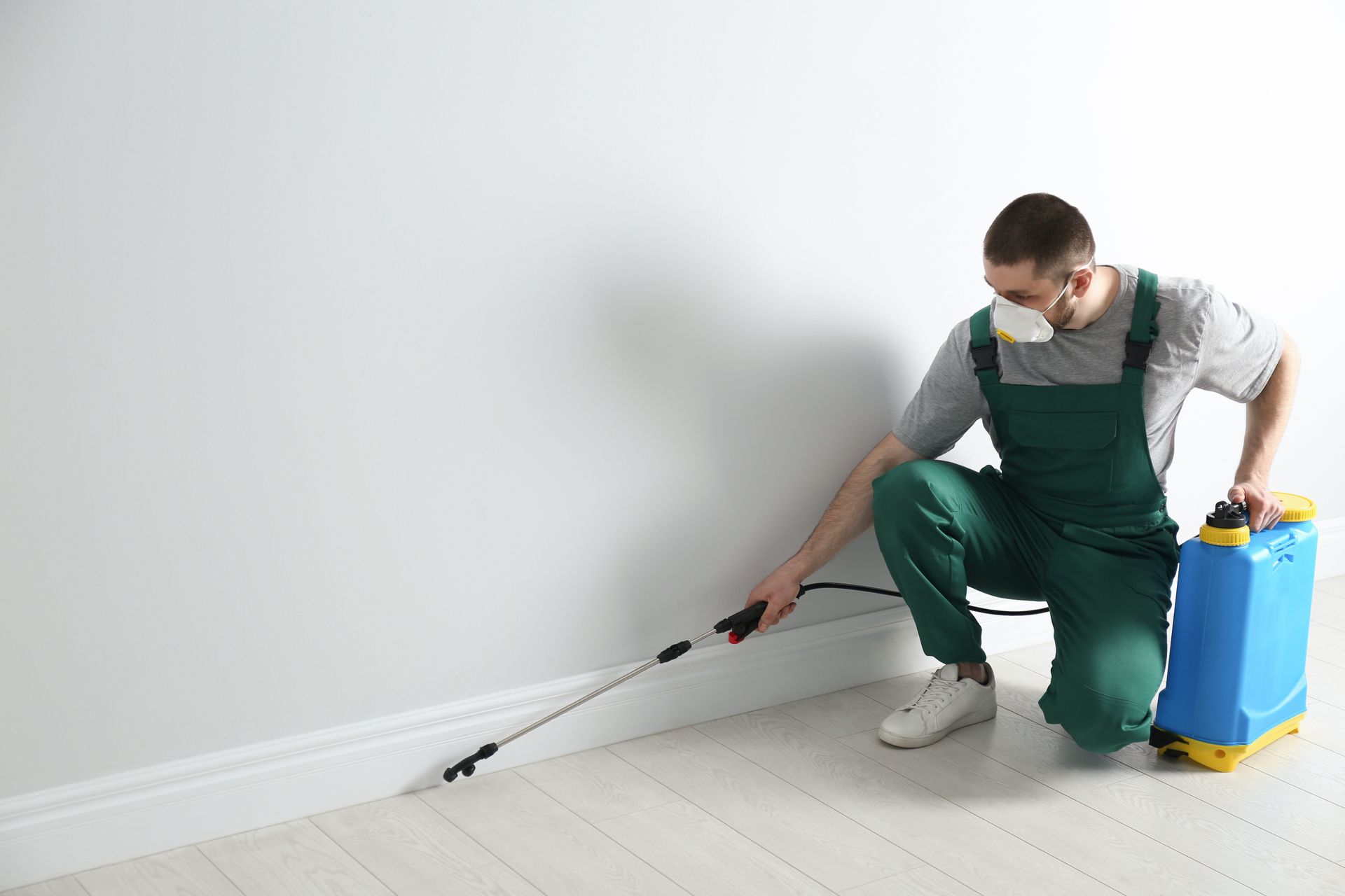 Pest control worker in uniform spraying pesticide indoors.