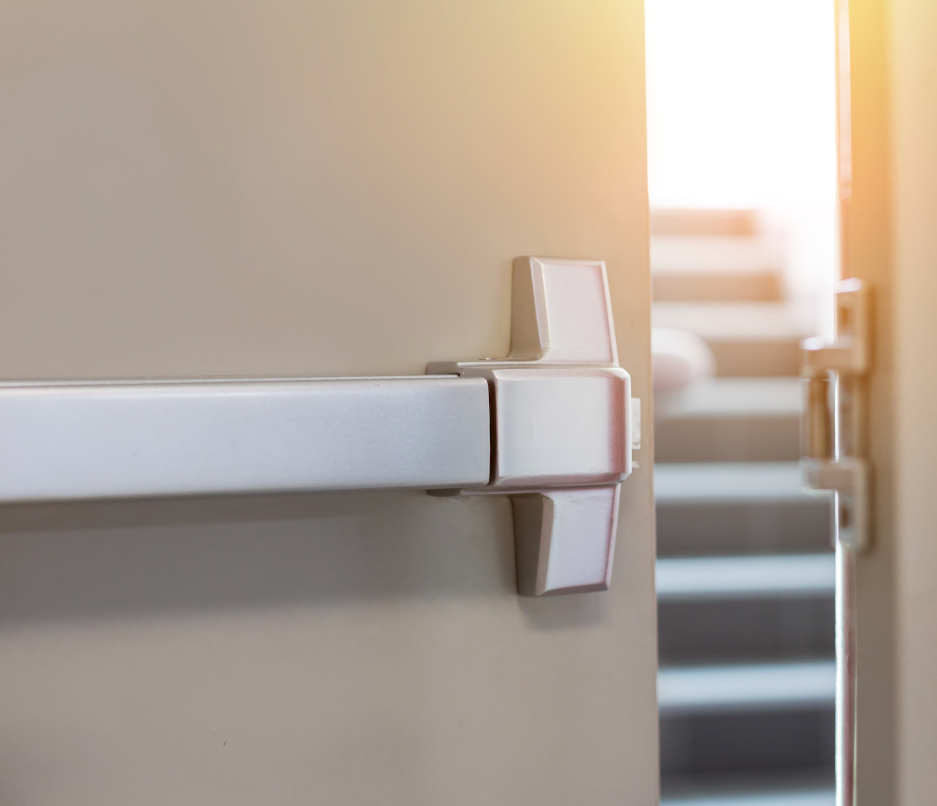 A close up of a panic bar on a door with stairs in the background.