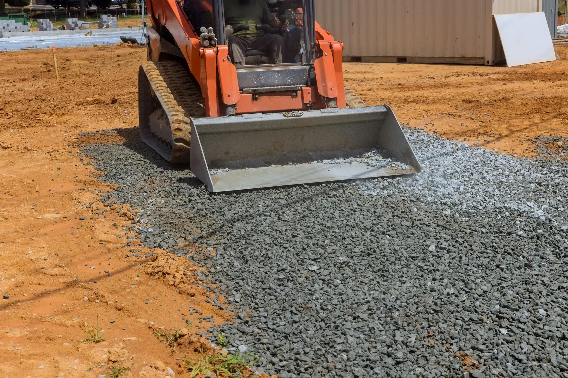 Orange skid steer spreading gravel on a dirt construction site