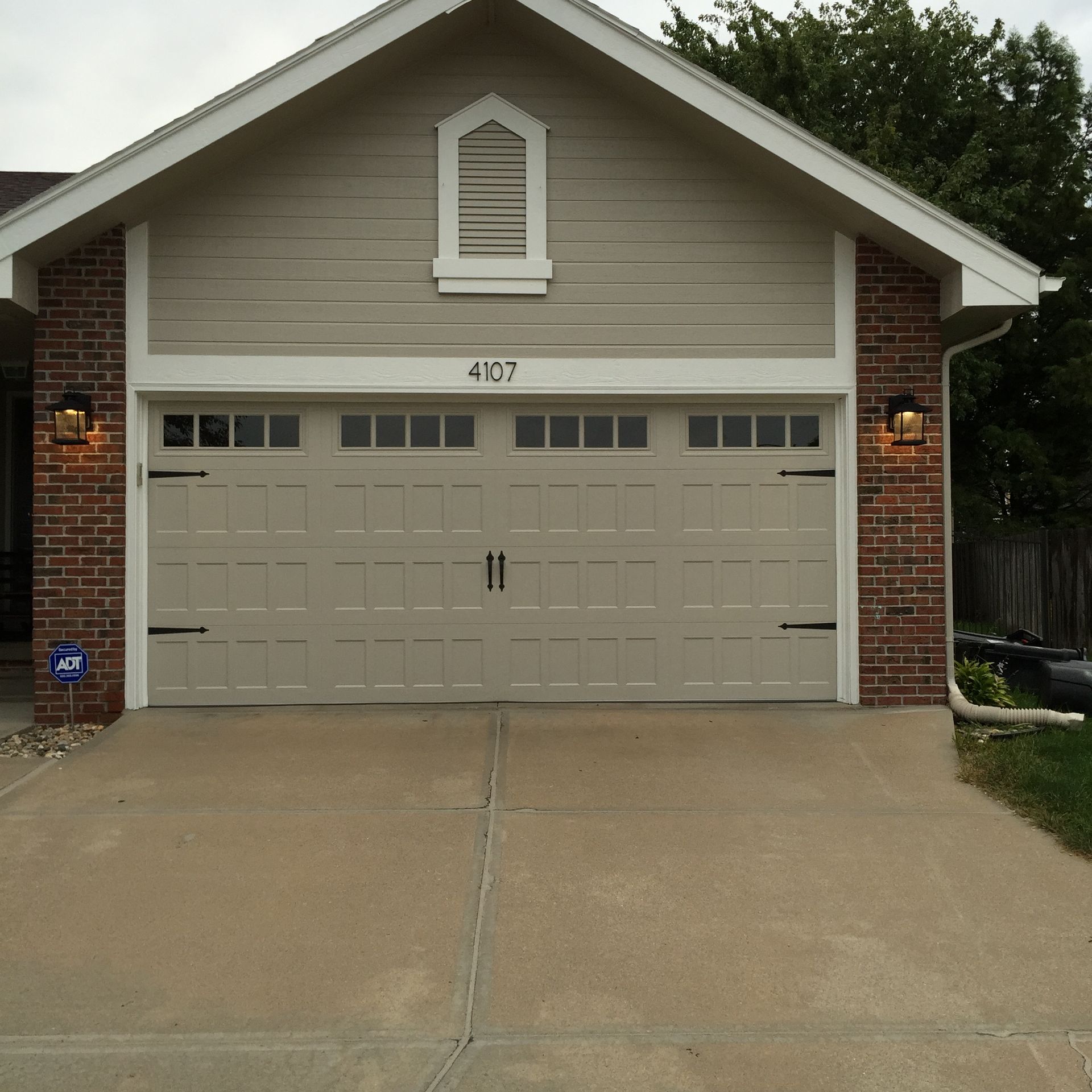 Suburban two-car garage with beige doors, brick accents, and a concrete driveway.