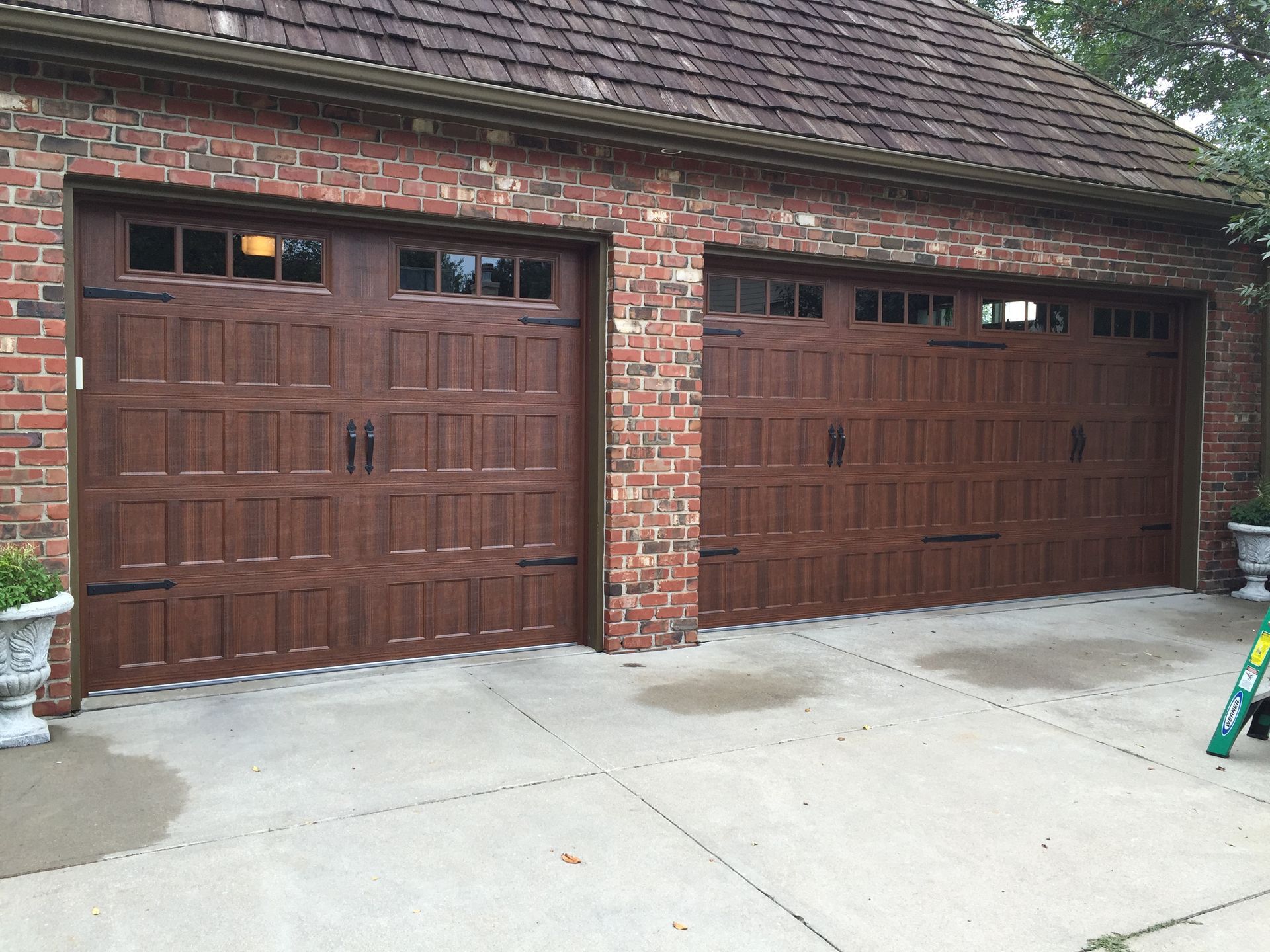 Two brown wooden garage doors on a brick house with a concrete driveway