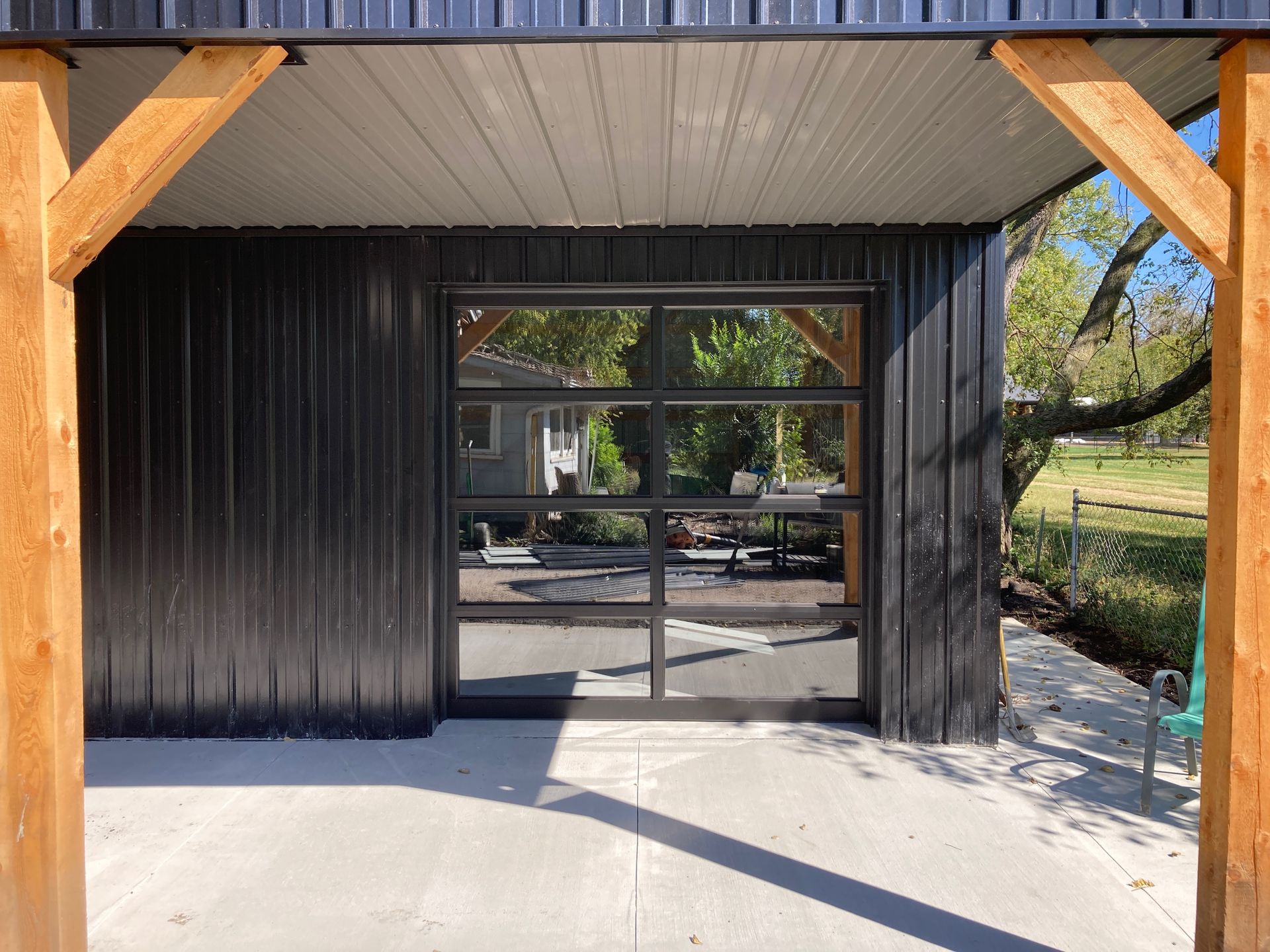 Black metal gate under a wooden roof, opening to an outdoor patio and yard.