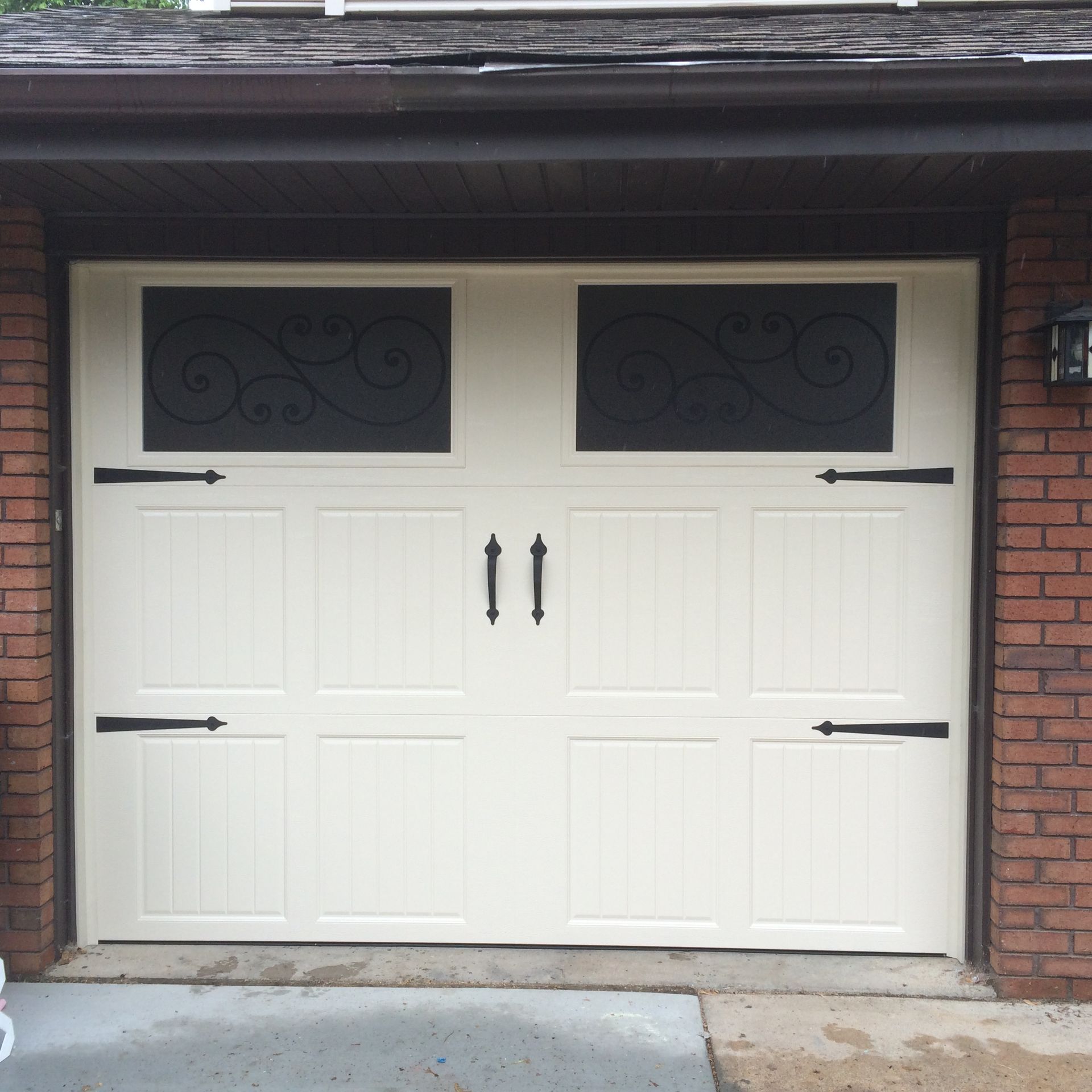 White double garage door with black handles, windows, and hinges set in a brick exterior.