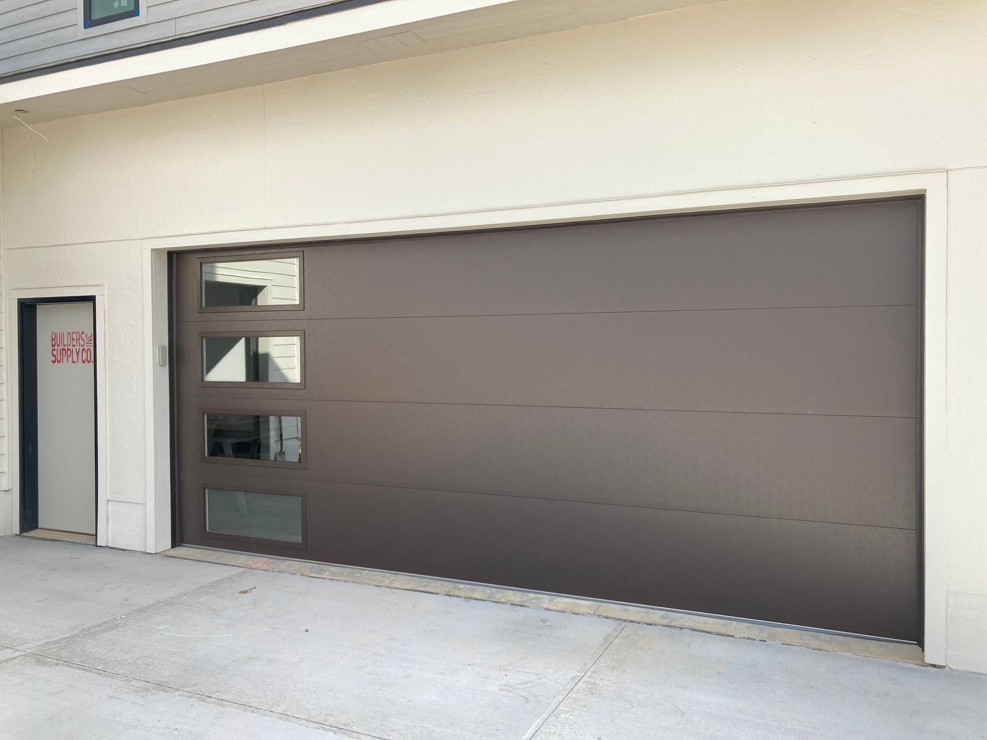 Modern building exterior with a large dark garage door and concrete sidewalk
