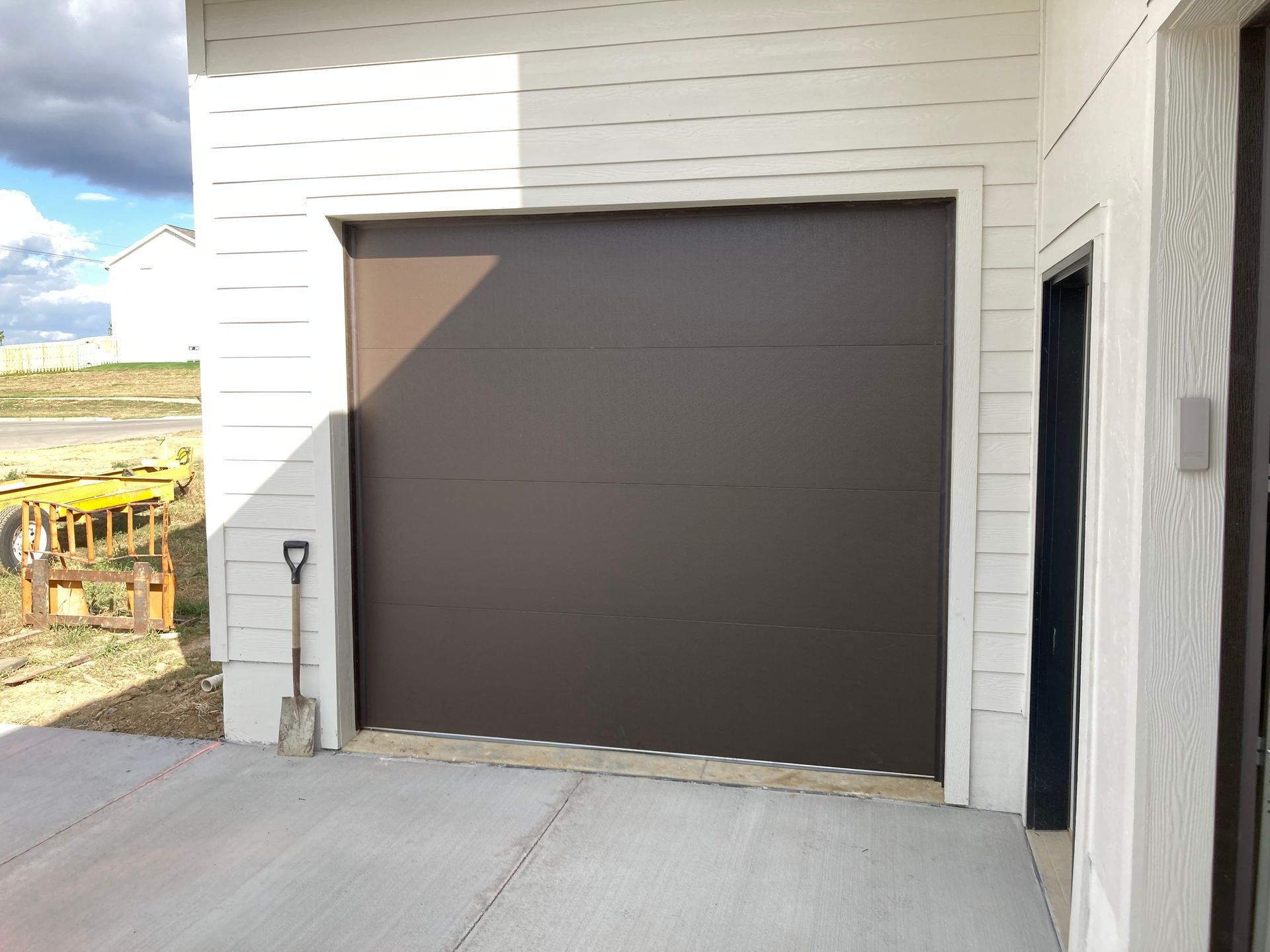 Closed brown garage door on a white house exterior with a concrete driveway.