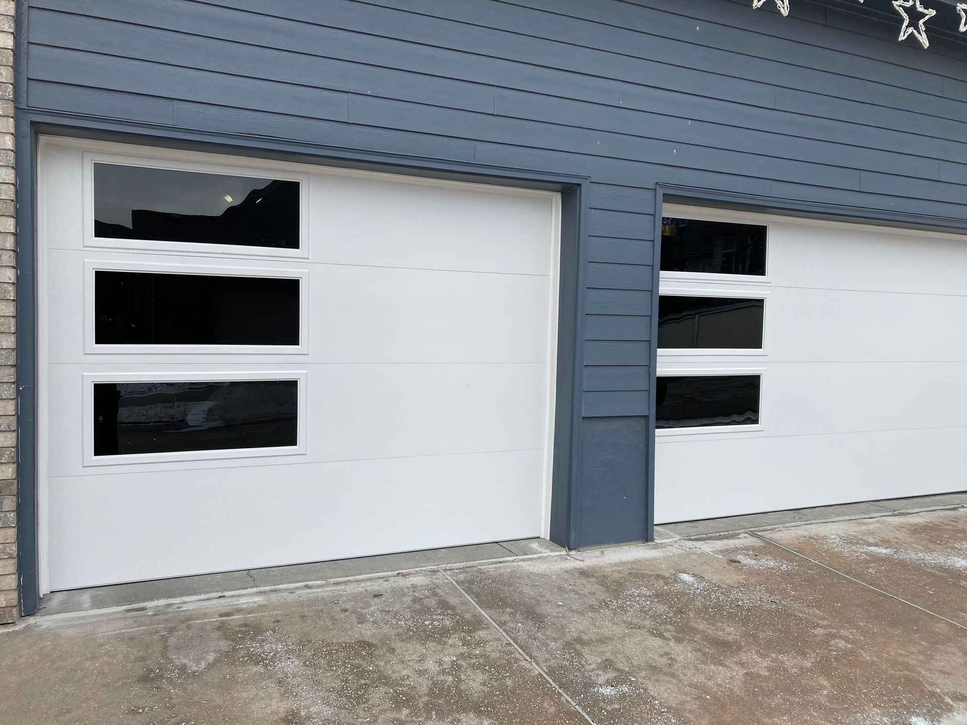 Blue house exterior with two white garage doors, each with small black window panels.
