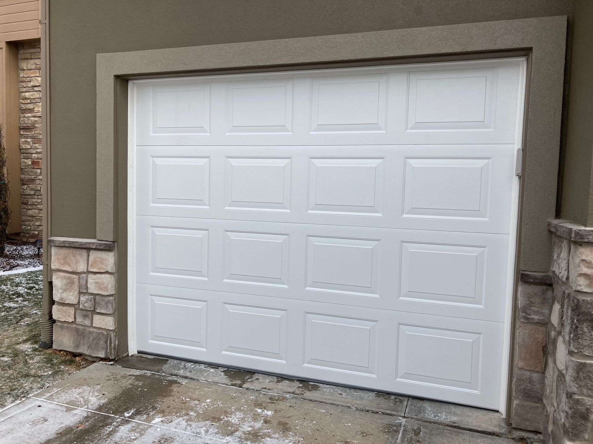 White double garage door with raised panel design set in a beige stone exterior.
