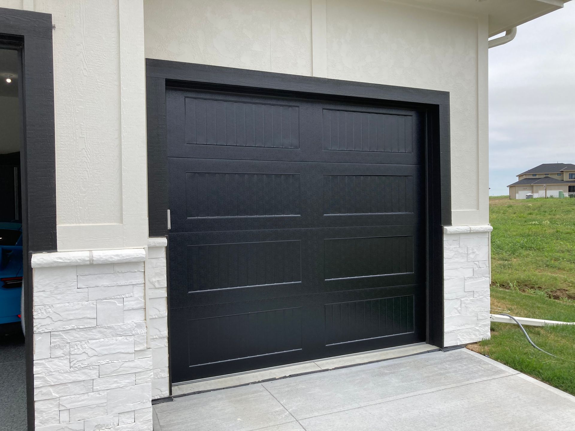 Black garage door on a modern house exterior with white stone trim and a driveway.