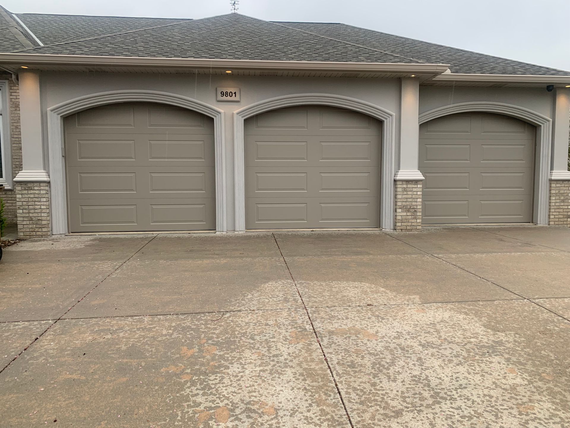Three beige garage doors on a stucco house with a concrete driveway in front.