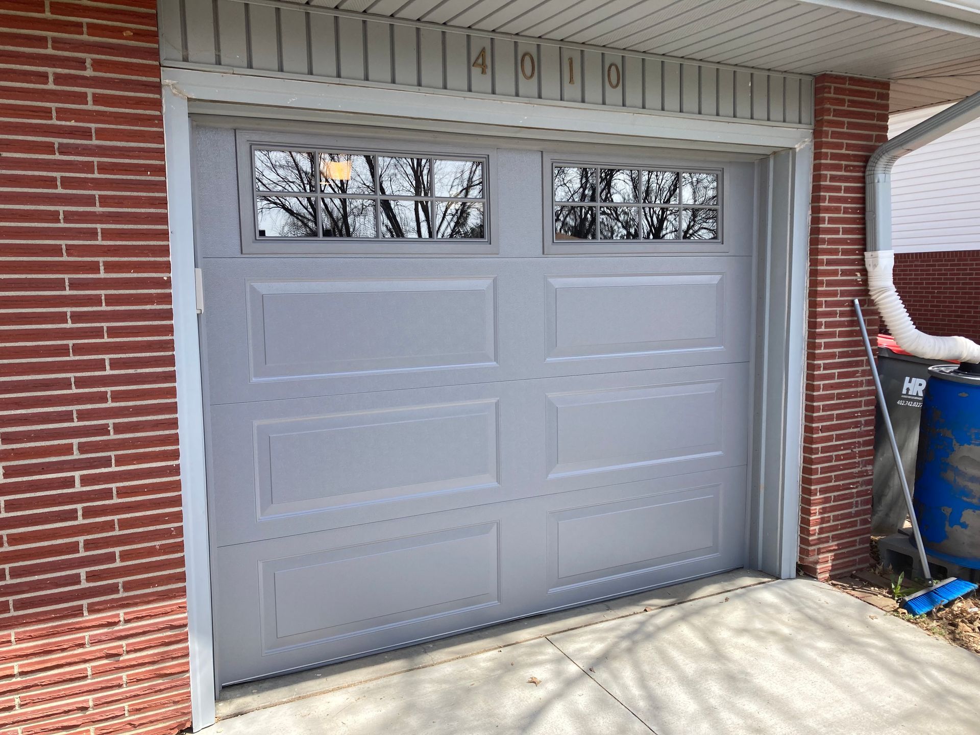 Closed gray garage door with small upper windows, set in a red brick exterior.