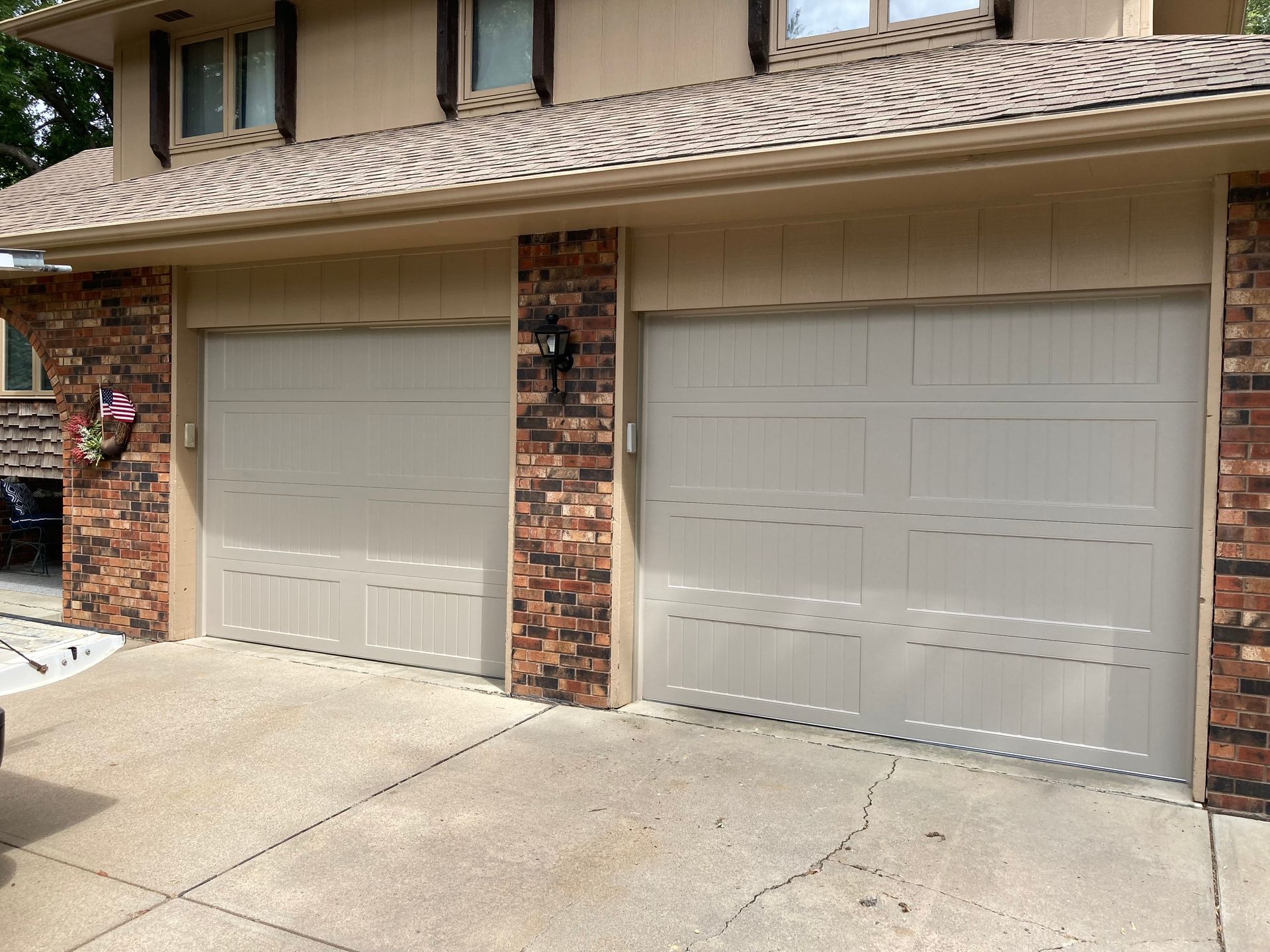 Two beige garage doors on a brick house with a concrete driveway