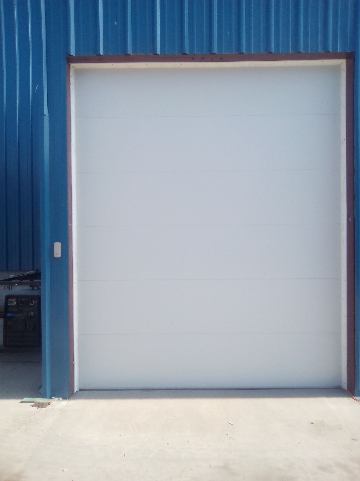 White roll-up garage door in a blue corrugated metal wall
