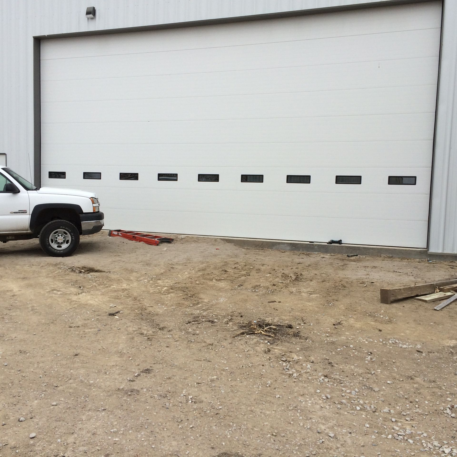 White industrial garage door with a pickup truck parked beside it on a gravel lot.