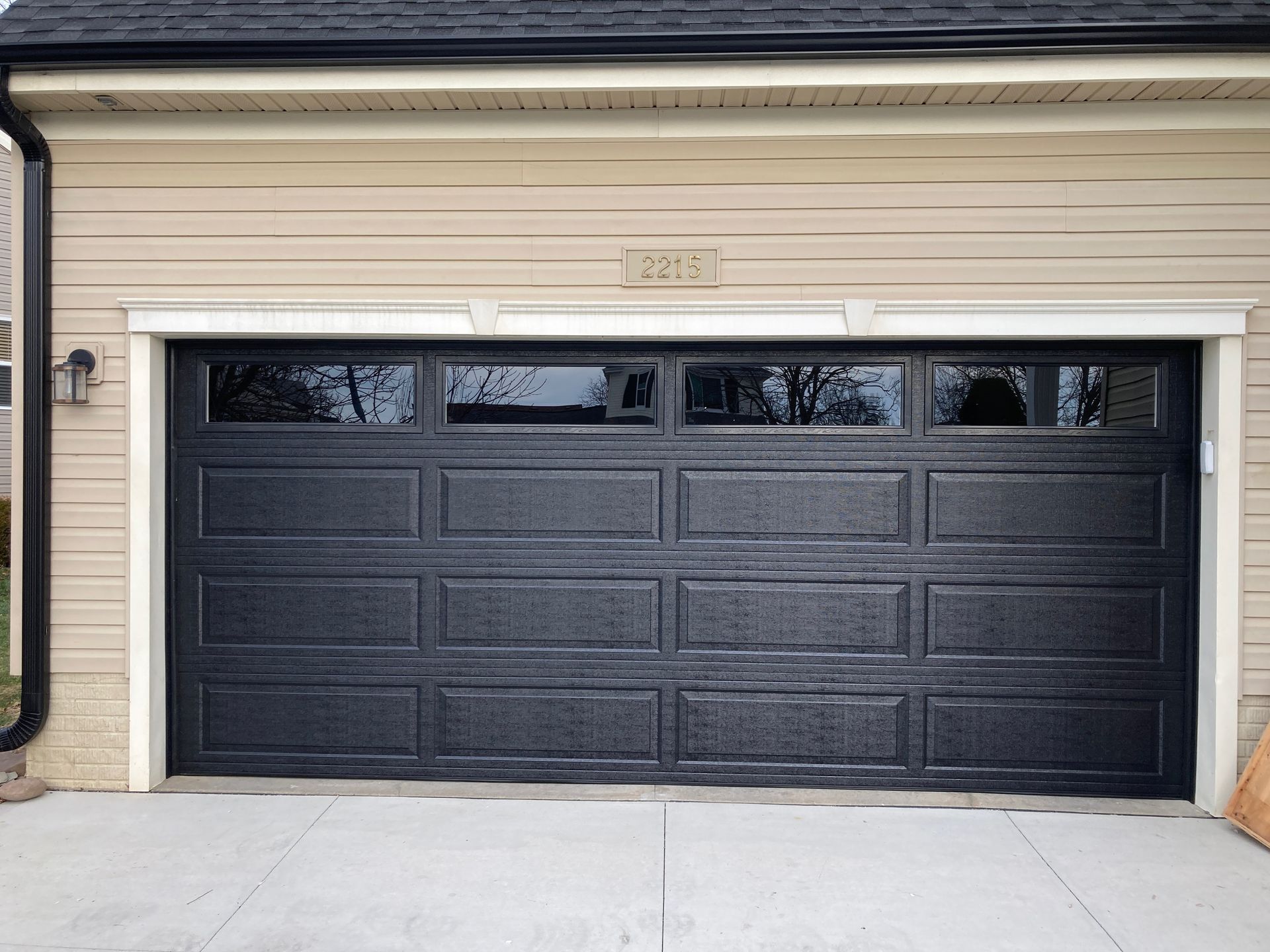 Black garage door on a beige house exterior with a concrete driveway